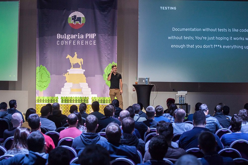 Phil standing on stage at Bulgaria PHP conference, pointing at his head for some reason